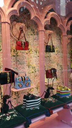 several purses and handbags are on display in a store window with floral wallpaper