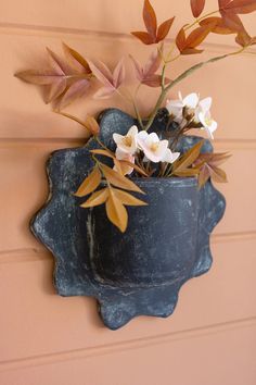 there is a blue vase with flowers in it hanging from the side of a wall