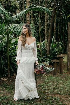 a woman in a wedding dress standing in front of trees and greenery with her hand on her hip