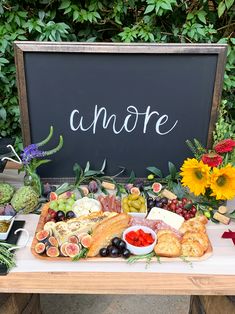 a wooden table topped with lots of different types of food next to a chalkboard