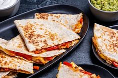 several quesadillas on black plates with guacamole in the background