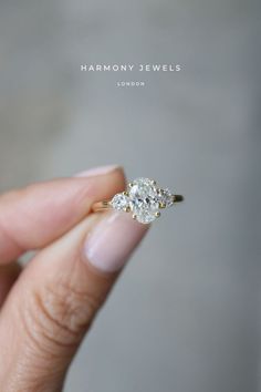 a woman's hand holding an engagement ring with two diamonds on it and the words harmony jewels