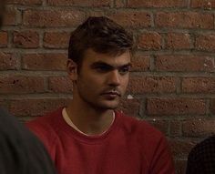 two men sitting next to each other in front of a brick wall with one man looking at the camera