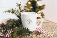 a white coffee mug sitting on top of a table next to a christmas tree and plaid napkin