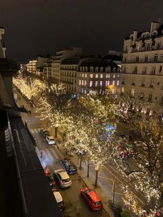 a city street filled with lots of traffic next to tall buildings covered in christmas lights