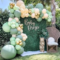 a baby shower backdrop with balloons and greenery in the shape of an arch is shown