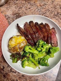 a white plate topped with steak and broccoli on top of a marble counter