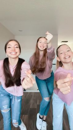 three girls are standing in the middle of a room with their arms up and thumbs up