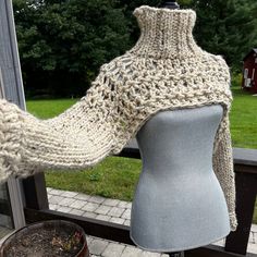 a mannequin with a knitted sweater on it's back, next to a window