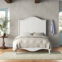 a white bed in a bedroom next to a wooden table and chair with a potted plant on it