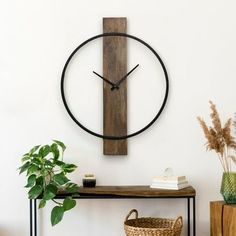 a wooden clock mounted to the side of a wall next to a table with a basket on it