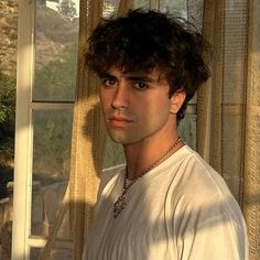 a man standing in front of a window wearing a white t - shirt and necklace