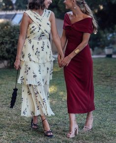 two women in dresses are holding hands and smiling at each other while standing on the grass