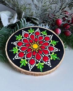 a decorated wooden slice sitting on top of a table next to evergreen branches and berries