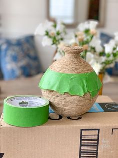 a vase sitting on top of a cardboard box next to a tape dispenser