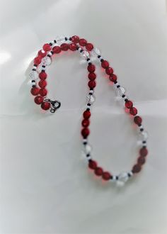 a red and white beaded necklace on a white surface with a silver charm hanging from it