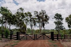 a dirt road with a wooden fence and trees in the background