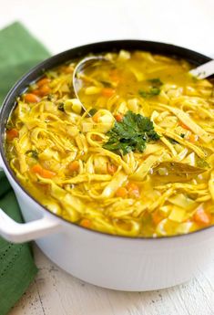 a white bowl filled with noodles and carrots on top of a green napkin next to a spoon