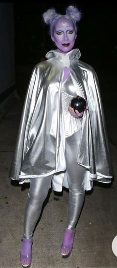 a woman dressed in silver and purple is walking down the street with her cat costume on