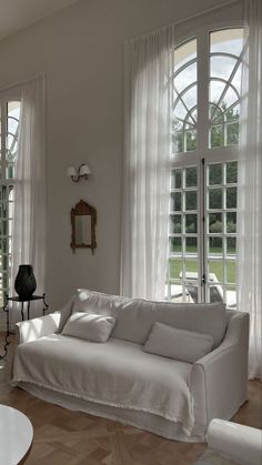 a living room filled with white furniture and large windows covered in sheered drapes