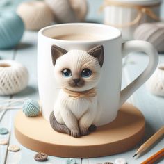 a cat figurine sitting on top of a coffee cup next to yarn balls