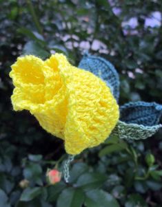 a crocheted yellow and blue flower with leaves in the background