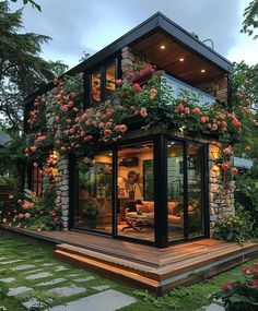 a small house with lots of flowers growing on the roof and windows in front of it