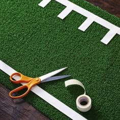 a pair of scissors sitting on top of a fake football field with tape and adhesive tape