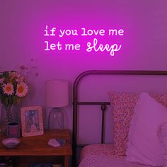 a bed room with a neatly made bed and a neon sign above it that says, if you love me let me sleep