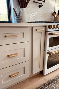 a kitchen with white cabinets and gold pulls on the drawers, an oven door is open