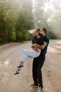 a man carrying a woman on his back in the middle of a dirt road surrounded by trees