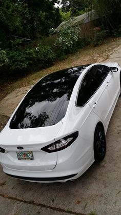 a white car parked on the side of a road next to some trees and bushes