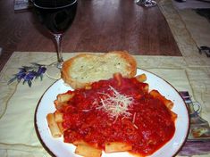 a plate with pasta, bread and tomato sauce on it next to a glass of wine