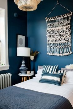 a bedroom with blue walls, white bedding and a large macrame hanging on the wall