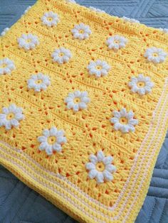 a crocheted yellow blanket with white flowers on the top and bottom, sitting on a quilted surface