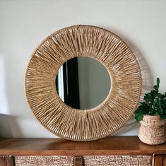 a round mirror sitting on top of a wooden dresser next to a potted plant