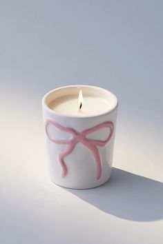 a white candle with pink bows on it and a single lit candle in the middle