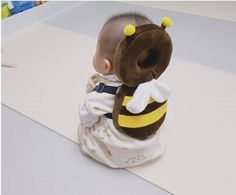 a baby sitting on the ground with a stuffed animal in it's lap and wearing a bee costume