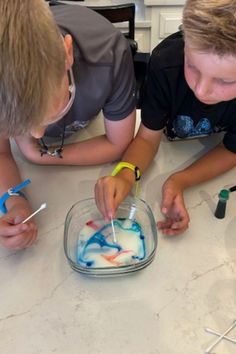 two young boys are decorating a cake with icing