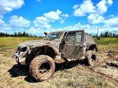 an off - road vehicle is stuck in the mud on a sunny day with blue sky and clouds