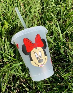 a plastic cup with a minnie mouse face on it is sitting in the green grass