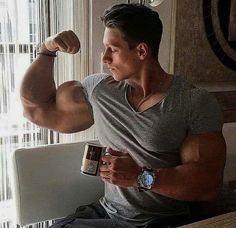 a man sitting at a table flexing his muscles and holding a coffee mug in front of him