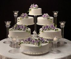 a wedding cake with purple and white flowers on the top is surrounded by wine glasses