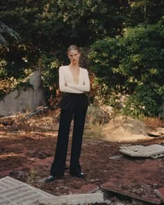 a woman is standing in front of some trees and rocks, with her arms crossed