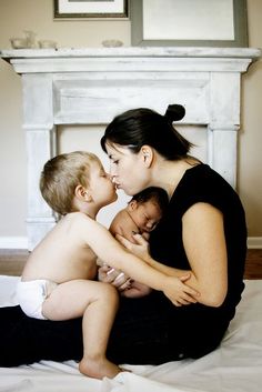 a woman sitting on top of a bed holding two babys next to a fireplace