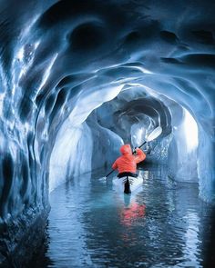 a person in a kayak paddling through an ice cave filled with blue water