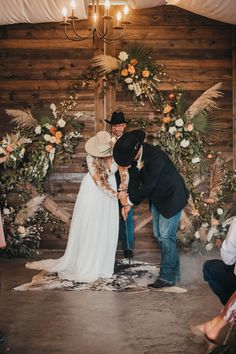 a bride and groom are kissing in front of an altar decorated with flowers, feathers and foliage