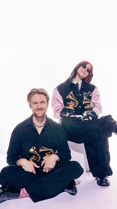 two people sitting on the ground with musical instruments in their hands and one person standing behind them