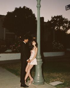 a man and woman standing next to a lamp post on the side of a street