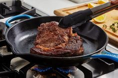 a steak being cooked in a skillet on top of the stove with tongs